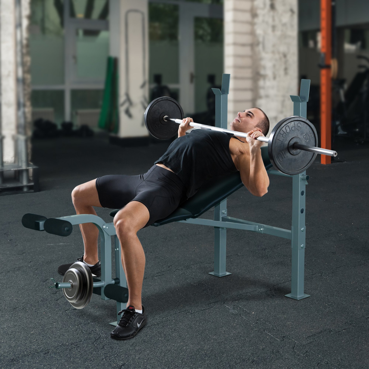 Man traint borst en benen op Verstelbare Halterbank met Beencurler – 165×68×114 cm – Zwart in sportschoolomgeving